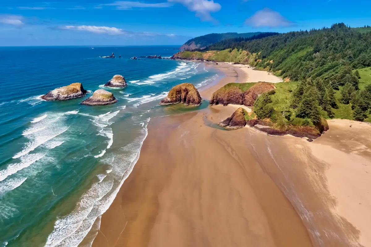 A peaceful exterior shot highlights rock formations, rolling waves, and a sandy beach bordered by forest. The open space and natural surroundings suggest a place to explore and unwind, with the beach easily accessible.