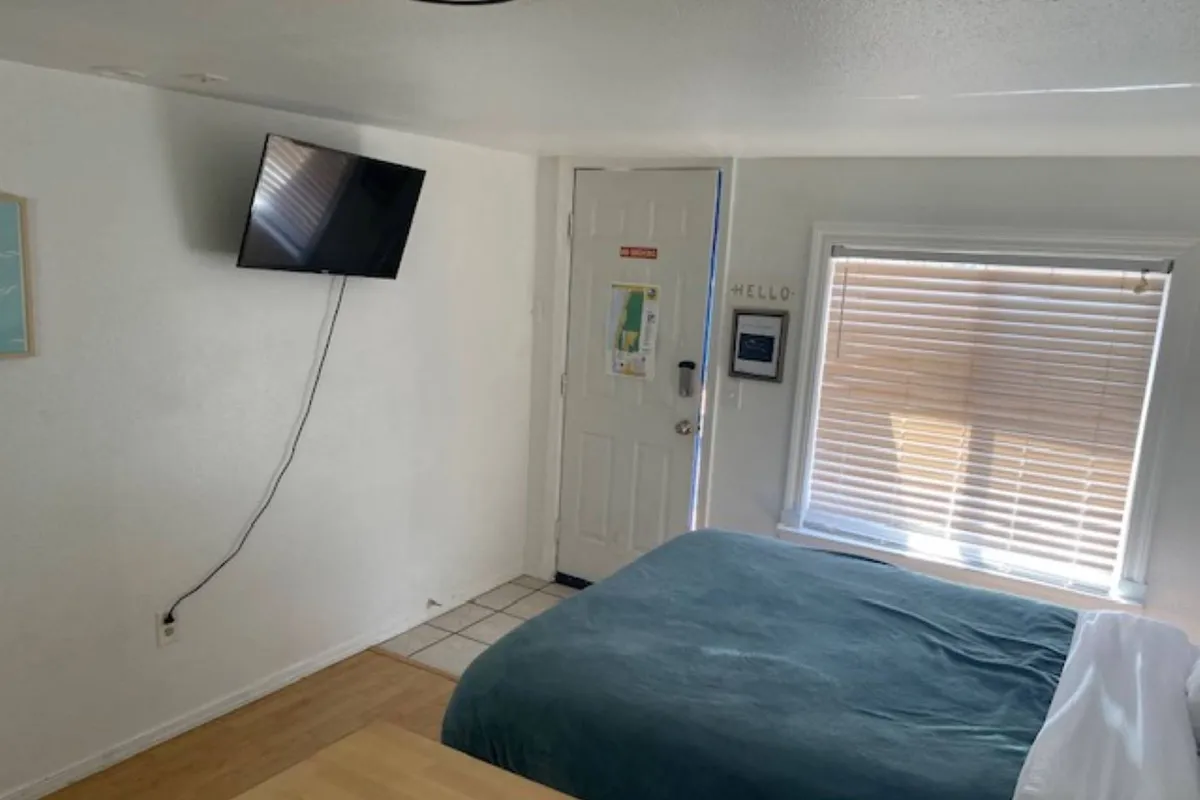 The image features the inviting interior of a one-bedroom condo at Sea Haven Motel, with a neatly made bed bathed in soft morning sunlight, a TV perfectly situated for cozy evenings, and a window offering glimpses of the peaceful surroundings—creating a tranquil space for relaxation or quiet moments.