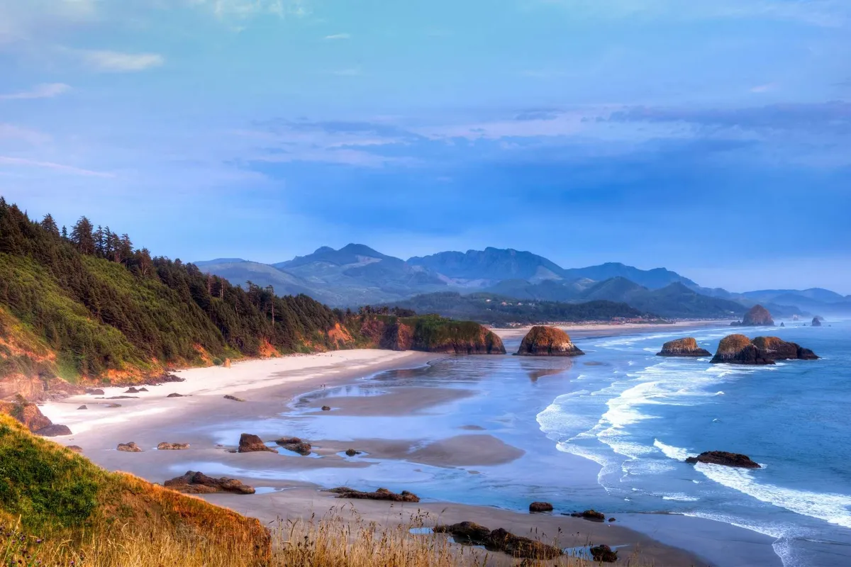 This image showcases a tranquil view of the ocean, rock formations, and the sandy beach meeting the sky. The scene is open and serene, evoking a sense of calm and natural beauty. The proximity to the beach is evident, suggesting an inviting environment just steps from the unit.