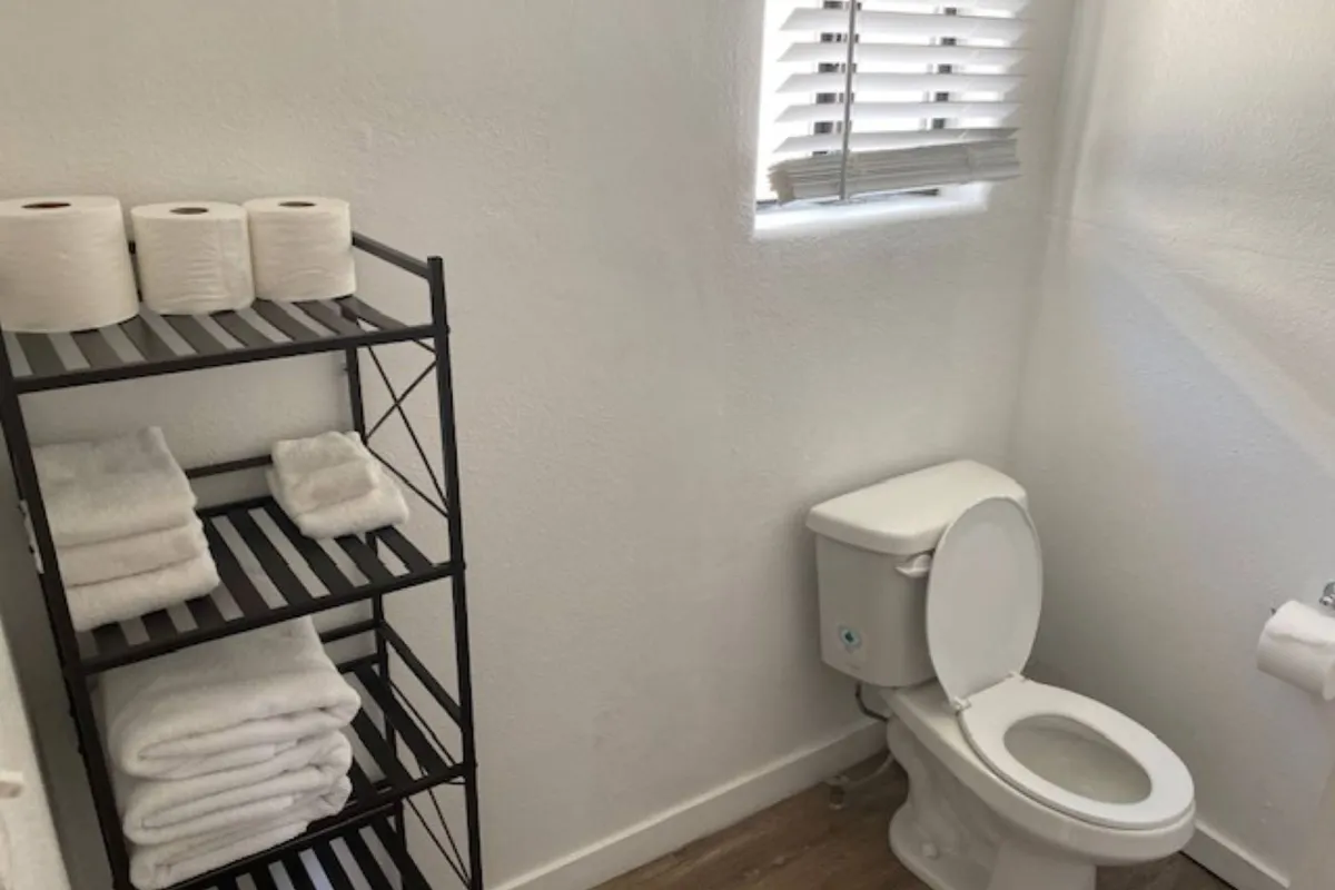 This serene interior image highlights the bathroom area with a toilet, towel rack, and shelves stocked with towels and toilet paper. The calming, uncluttered scene suggests a space for relaxation and self-care.